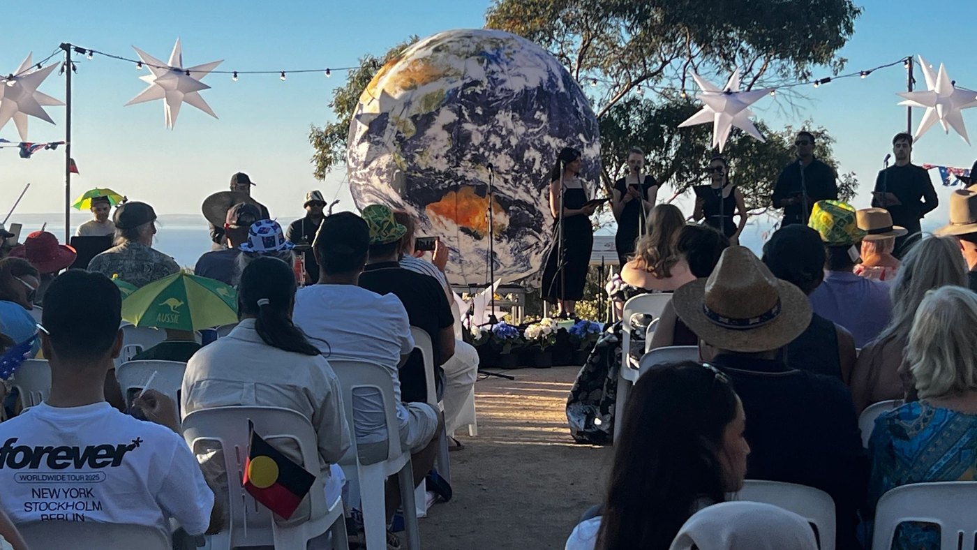 Audience seated before the illuminated Earth globe as singers perform at the Australia Day ceremony