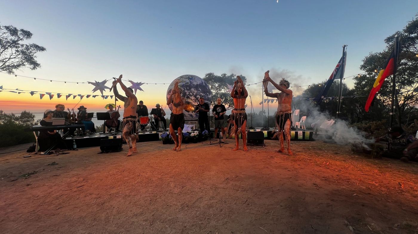 Australia Day ceremony at sunset with performers and flags overlooking the bay