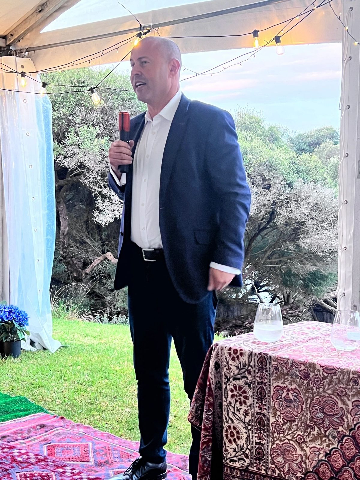 Guest speaker in a navy blazer addressing an outdoor evening garden talk